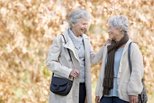 Senior friends, happy and conversation in park by autumn leaves, together and bonding in retirement in outdoor. Elderly women, smile or communication on vacation in england, care or travel in nature.