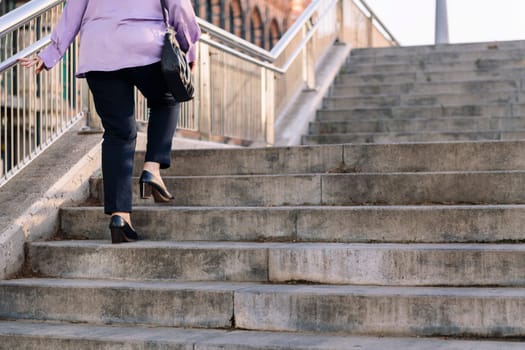 legs of senior woman walking up stairs at city