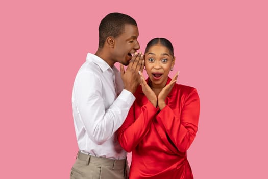 Black man whispering secret to surprised woman
