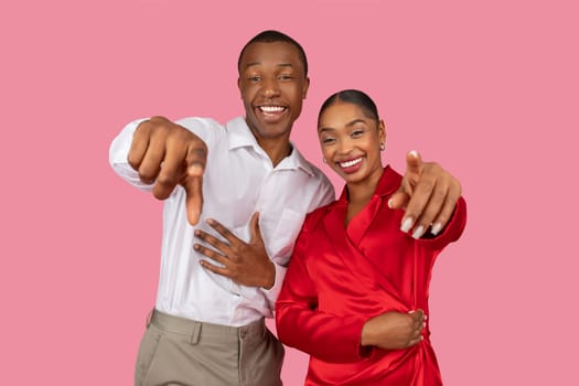 Joyful african american couple pointing at camera with friendly gesture