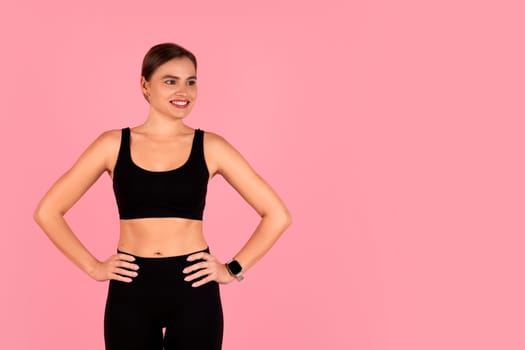 Smiling woman dressed in black workout clothes standing with hands on hips