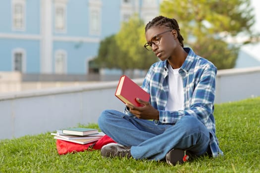 Thoughtful African American guy holding book outdoor at campus park