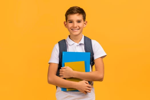 Smiling teen schoolboy with backpack holding textbooks and smiling at camera
