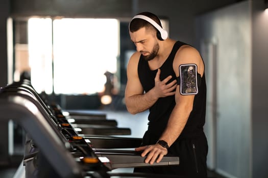 Distressed man experiencing sudden heartache while working out on treadmill at gym