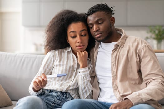 Stressed unhappy black couple looking at pregnancy test result indoors