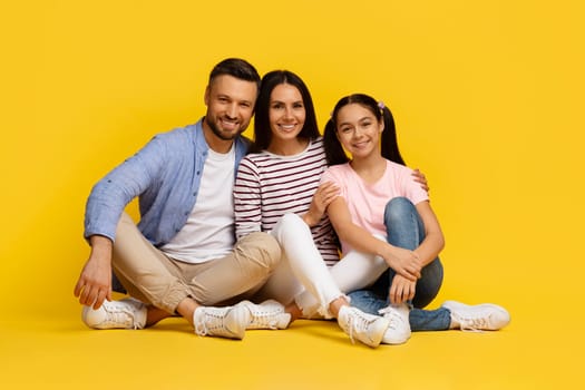 Happy caucasian family of three sitting on floor and embracing