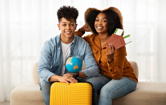 Smiling young african american couple in hat, with suitcase, show passport and tickets