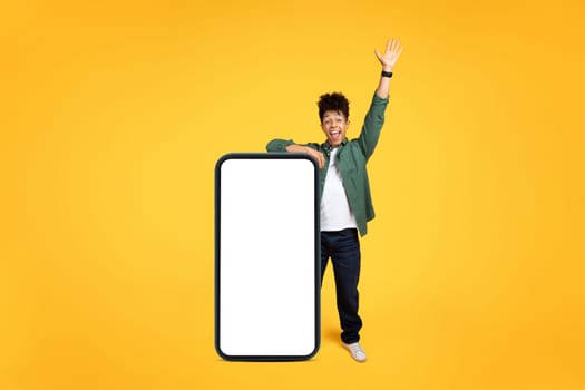 Joyful young black guy stand by huge phone, gesturing
