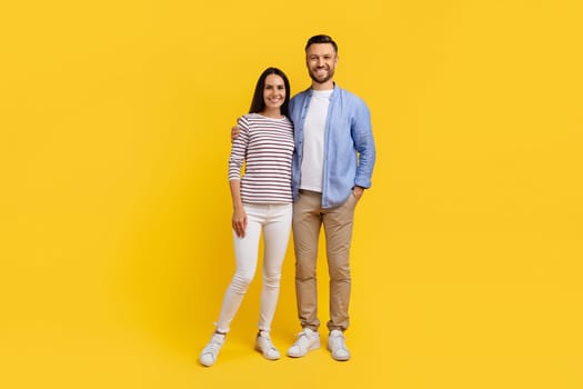 Portrait of smiling caucasian couple in casual clothes standing against yellow background