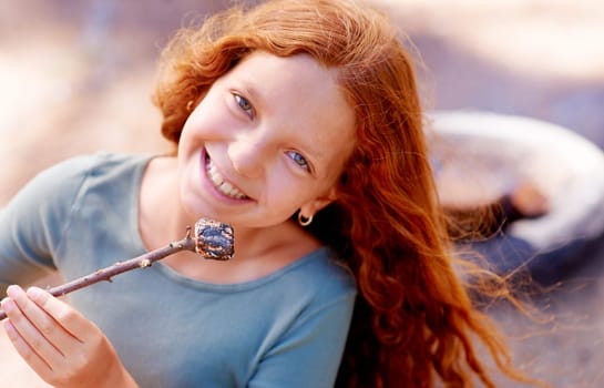 Young girl, camping and marshmallow in portrait with smile, nature and sweet snack in woods. Red hair, teenager and happiness on face for sugar candy, relax and outdoor on holiday adventure by fire