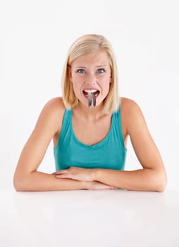 Woman, portrait and eating a fish, tail or strange food in mouth on white background of studio. Crazy, diet and person with weird seafood, cuisine and face of disgust for taste of tuna or salmon.