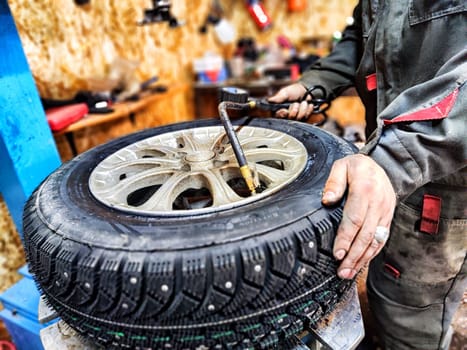 Ishim, Russia - November 27, 2023: A mechanic repairs a car wheel and makes a tire in a dirty garage. Replacement of summer wheels, tires for winter indoors