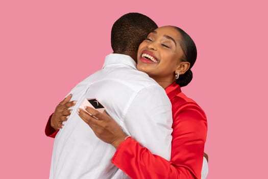 Black woman joyfully hugging man after proposal, ring shown