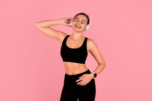 Happy young woman in sportswear and wireless headphones dancing and enjoying music
