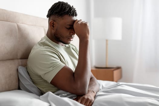 Unhappy black man in bed pressing fist to forehead indoor