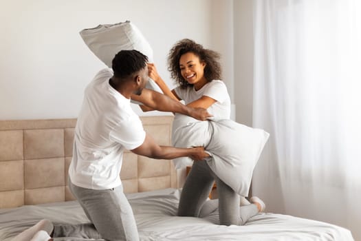 Playful african spouses having fun in bedroom enjoying pillow fight