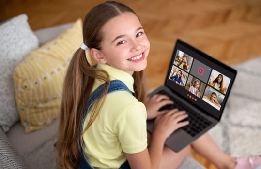 Smiling girl pupil sitting on couch at home, using laptop