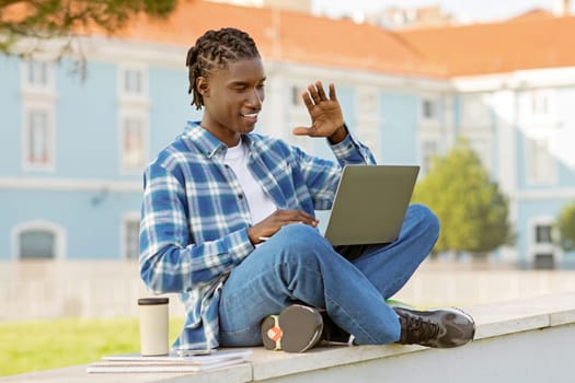 African student waves hello during video call on laptop outdoors
