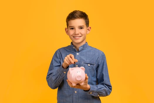 Smiling young boy in blue shirt depositing coins into pink piggy bank