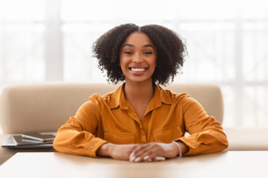 Smiling pretty curly young african american lady sit at table, enjoy free time