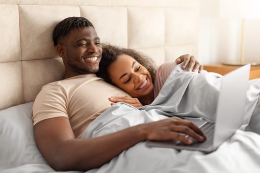 Cheerful African American Couple Watching Movie On Laptop In Bed