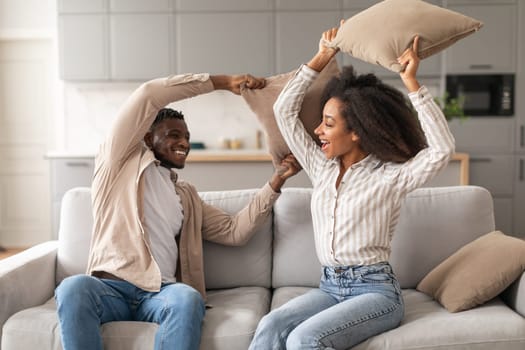 Joyful Black Millennial Couple Having Pillow Fight In Living Room