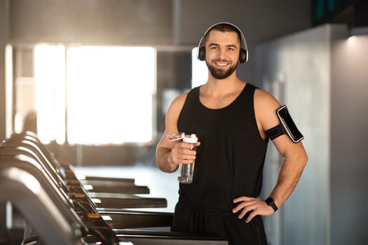 Smiling bearded man with headphones and arm band standing on treadmill