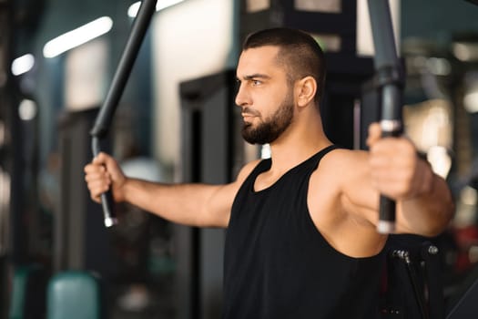 Concentrated man in tank top exercising on chest press machine at gym