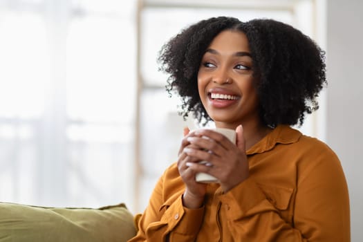 Glad pensive millennial black lady enjoy cup of coffee in hands, free time