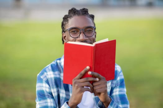 Portrait Of Black Student Guy In Eyeglasses Reading Book Outside