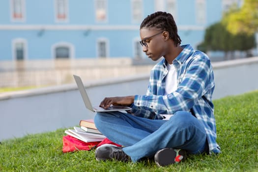 Focused black guy engages in e-learning on his laptop outdoor
