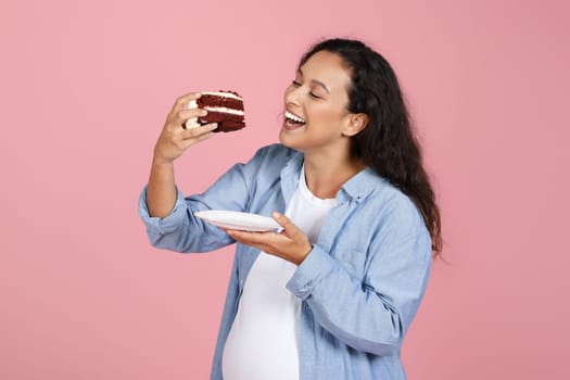 Excited Pregnant Lady Eating Cake Standing Over Pink Studio Background
