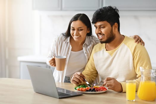 Happy young indian family using laptop while have breakfast