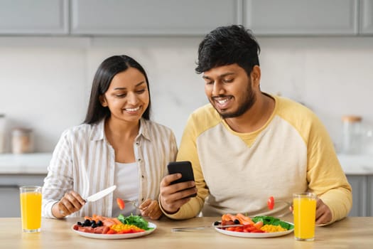 Beautiful loving young eastern couple scrolling while have breakfast
