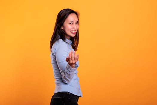 Smiling cheerful asian model doing come to me symbol