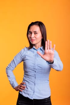Serious asian woman raising palm to advertise stop gesture