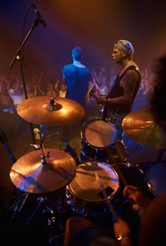 Drummer, musician and band at stage for concert, performance and crowd at night. Music festival, talent and people playing for audience in theater or club with instrument, light and creative energy