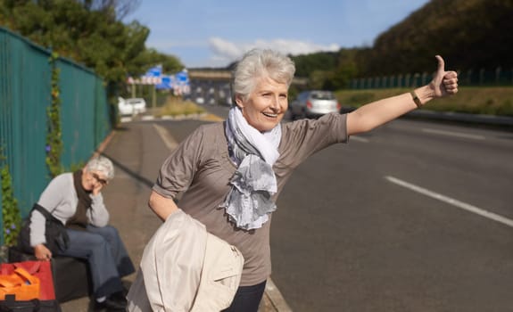 Women, road and hitch hiker for lift in retirement, travel and friends in city with bags for adventure. Senior ladies, thumbs up and happy by roadside with hand gesture and stop transport to commute.