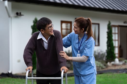 Nurse or caregiver helps elderly walk by using walker in garden