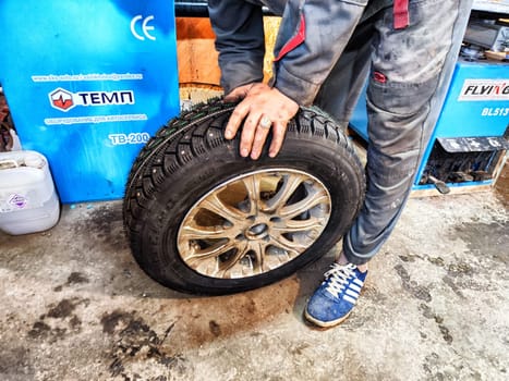 Ishim, Russia - November 27, 2023: A man makes tire of car wheel before cold snow season. Experienced mechanic changes wheel of car. The driver prepares a classic car for driving in the snow in winter