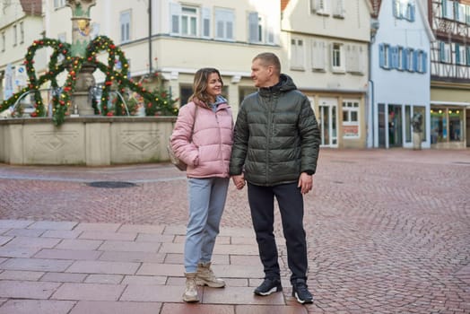 Loving couple of tourists walking around old town. Couple of lovers leisurely stroll in the cool autumn morning on the streets of a BIETIGHEIM-BISSINGEN (Germany). The guy holds his wife. Vacation, Winter, holiday. Romantic Stroll through Historic German Charm. Couple Walking in Europe's Old Town