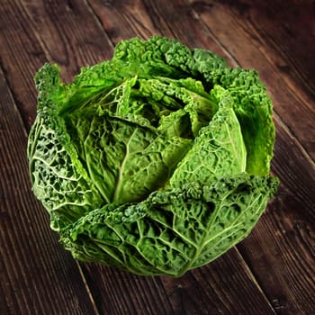 Single green savoy cabbage lettuce head on dark wooden board