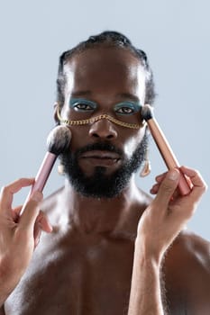 Bearded gay man applying makeup with brushes held by crop artist