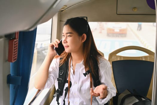 Happy young Asian woman talking on mobile phone while while traveling in bus. Travel lifestyle and transportation concept