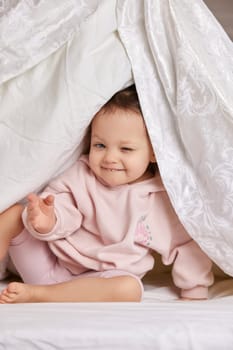 cute baby looks out from under the blanket