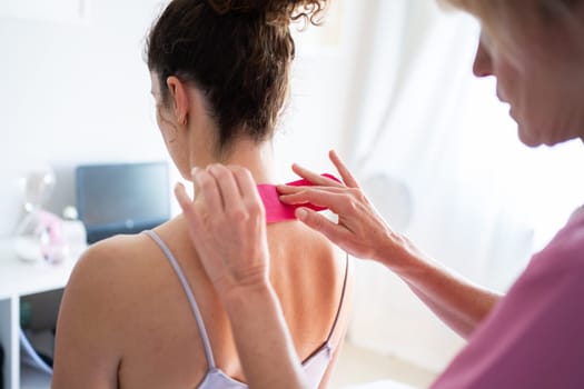 Woman applying soothing kinesiology tape on neck of client