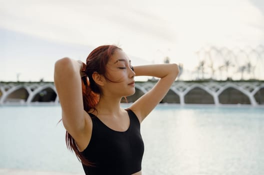 Young woman in sportswear standing with raised arms and have a rest after morning workout outside