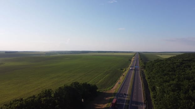 Aerial view on highway road through green fields on a summer sunny day. 4k footage of landscape with asphalt freeway between meadow and rural field. Drone shoots video of the countryside.