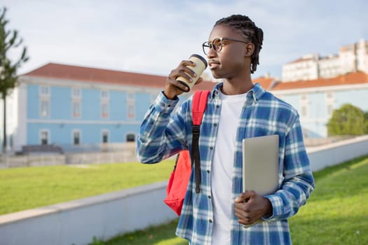Black student guy with backpack and laptop drinking coffee outdoors