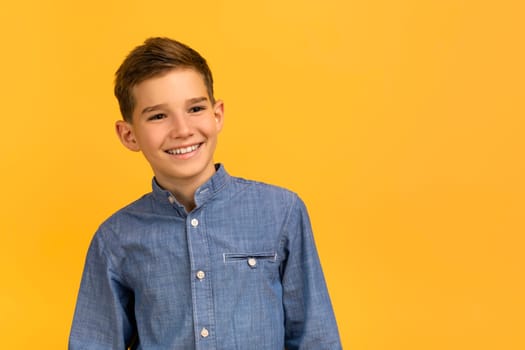 Happy teenage boy in denim shirt confidently posing on yellow studio background